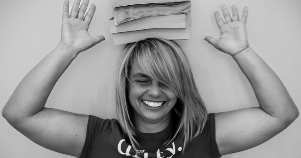 Coral Hart - romance author with 200+ novels - books balanced on head, laughing